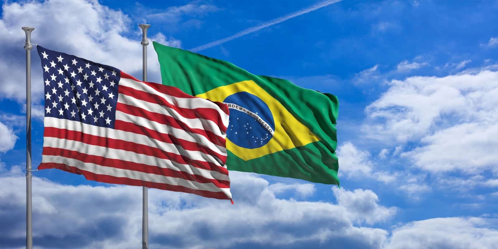 Bandeiras dos Estados Unidos e do Brasil tremulando lado a lado contra o céu azul