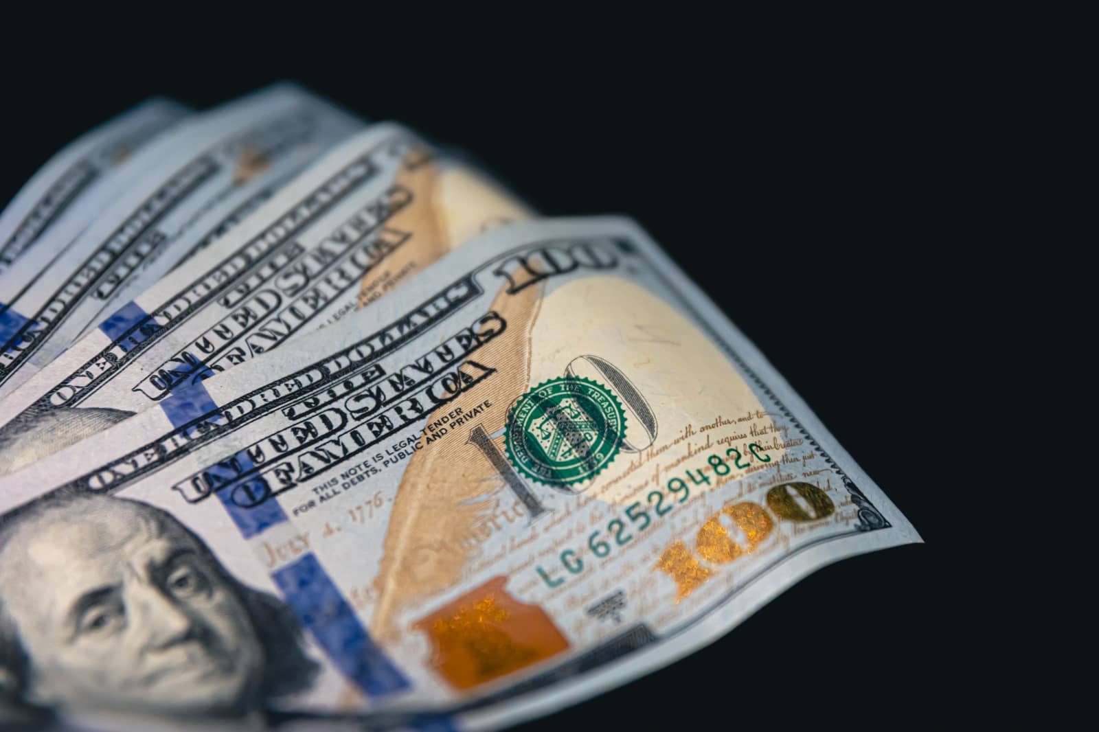 Notas de cem dólares americanos em close, dispostas em leque