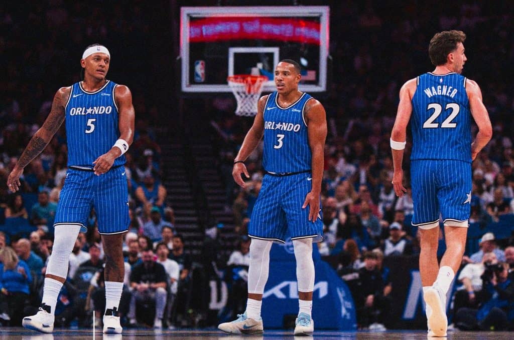 Três jogadores do Orlando Magic em quadra, com a torcida ao fundo