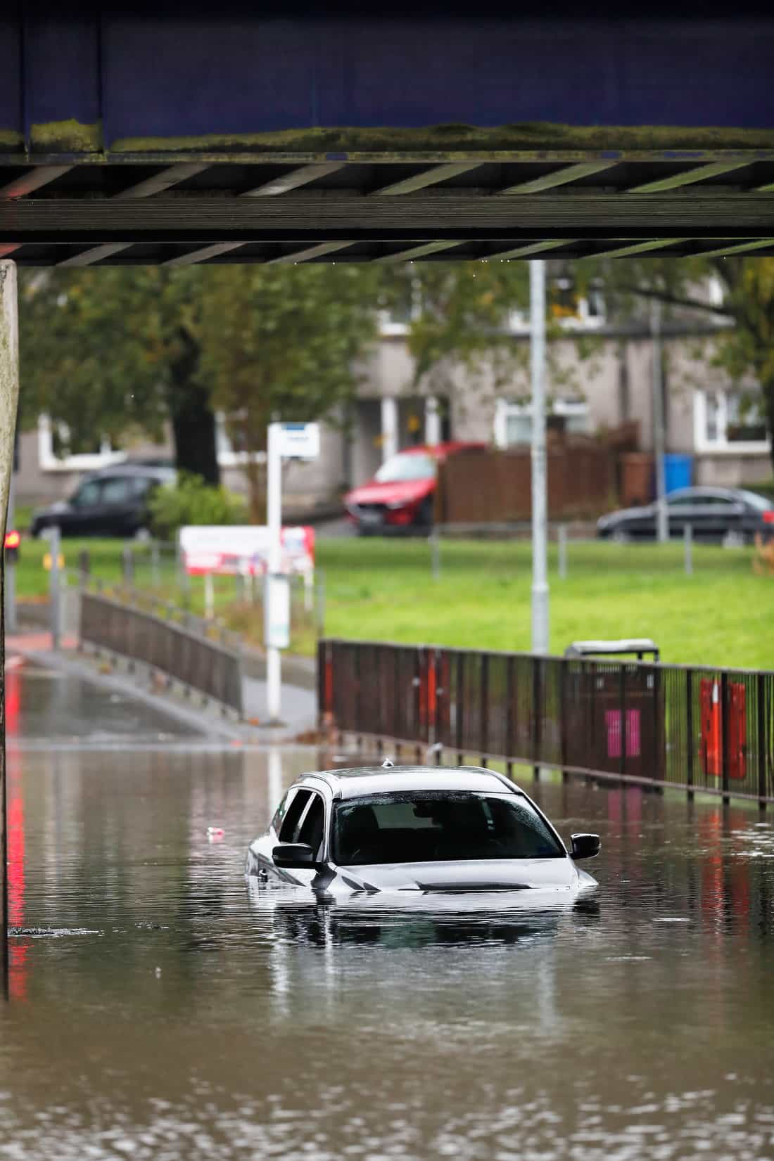 Carro quase todo submerso em uma rua alagada sob um viaduto