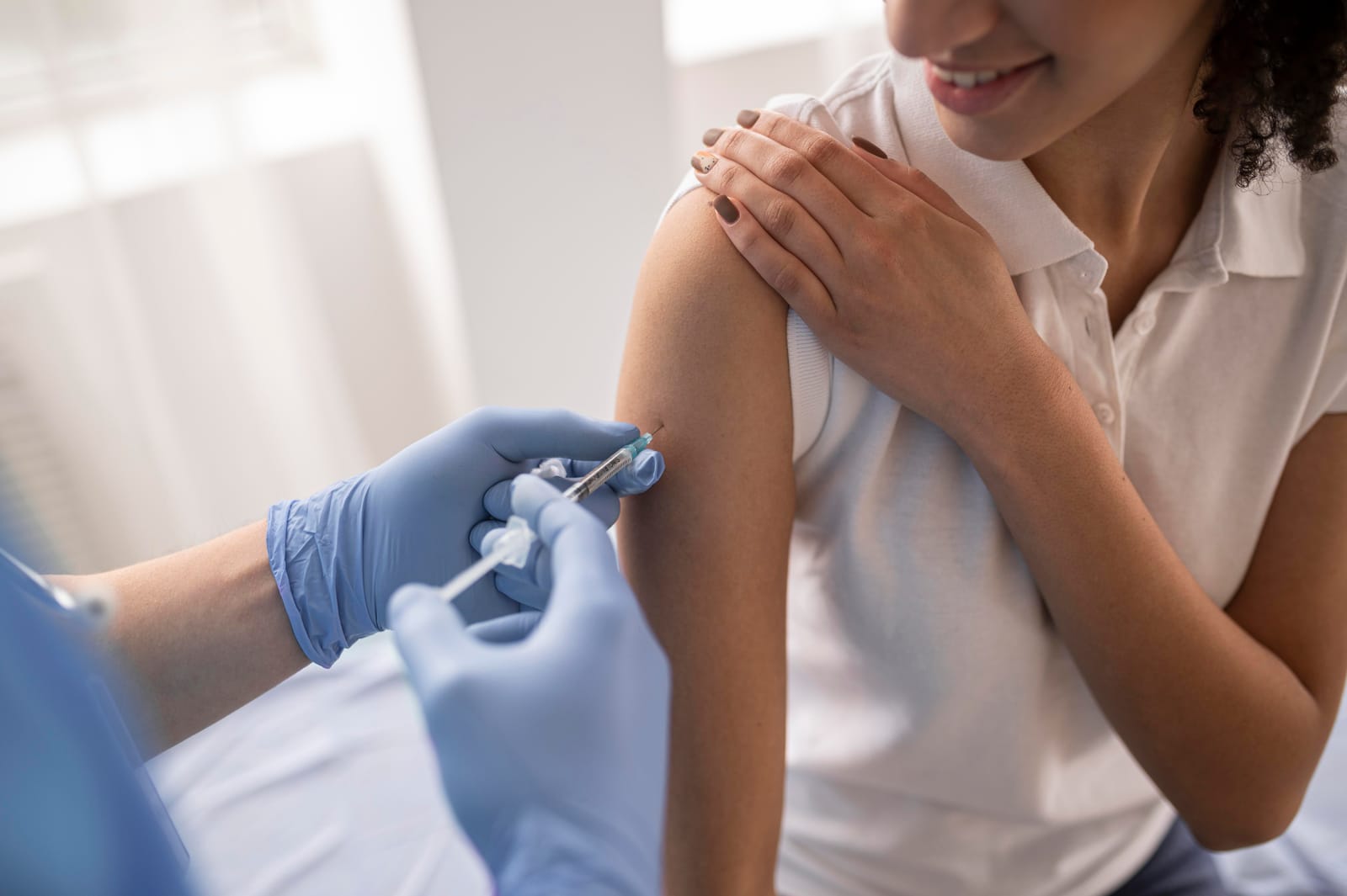 Profissional de saúde de luvas azuis aplica uma injeção no braço de uma mulher sorridente
