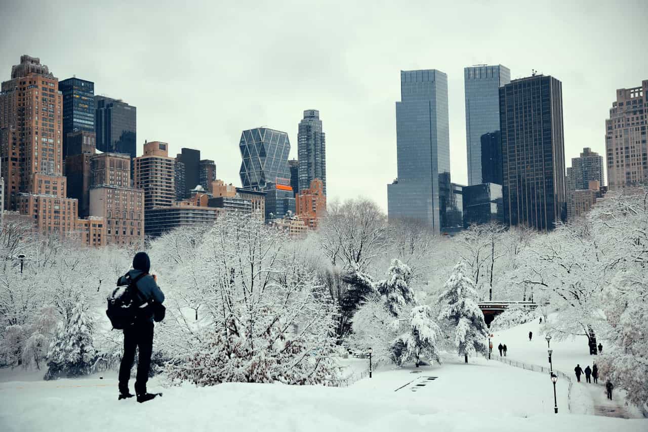 Homem fotografa o Central Park coberto de neve, com prédios de Nova York ao fundo